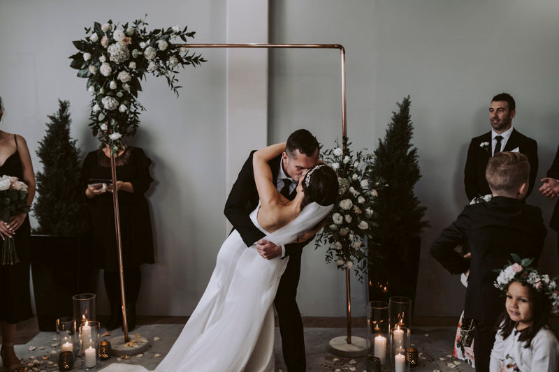 bride and groom kiss under wildrose florist designed arch at wedding